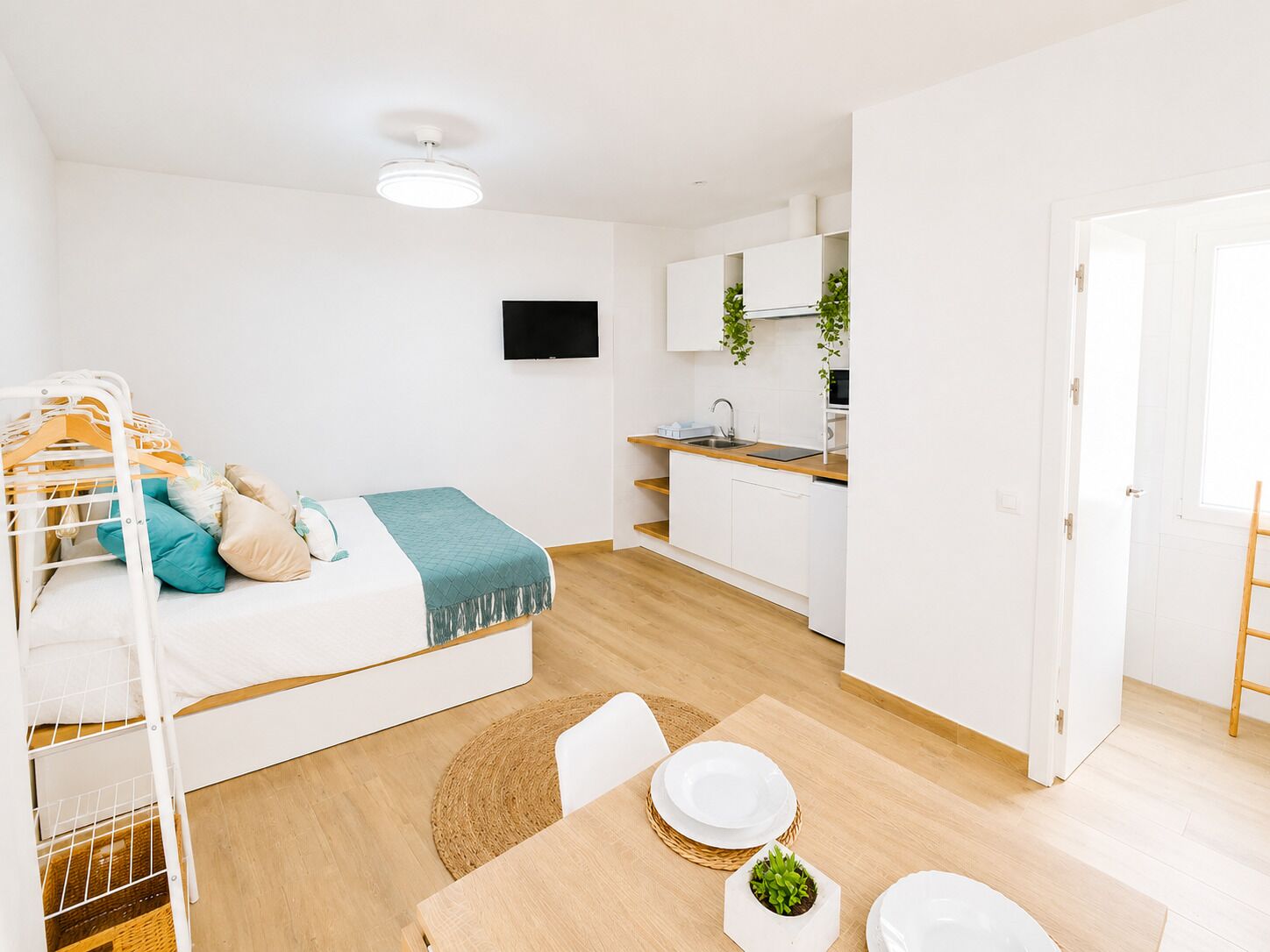A compact living space with a bunk bed, kitchenette, dining area, and a TV mounted on the wall.