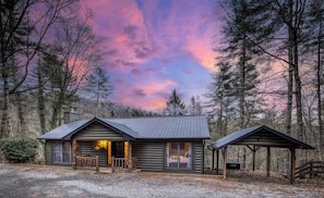 Eine Blockhütte mit Veranda, einem überdachten Picknickbereich und Blick auf den umliegenden Wald.