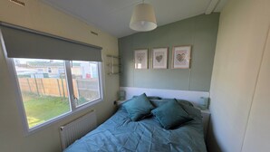 Ein Schlafzimmer mit einem Bett, einem Fenster, einem Heizkörper, einer Pendelleuchte und drei Wanddekorationen in Herzform.