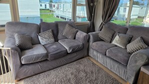 Ein Wohnzimmer mit zwei grauen Sofas, einem grauen Teppich und großen Fenstern mit Vorhängen.