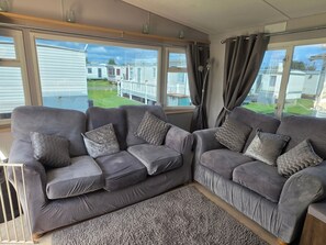 Ein Wohnzimmer mit zwei grauen Sofas, einem grauen Teppich und großen Fenstern mit Vorhängen.