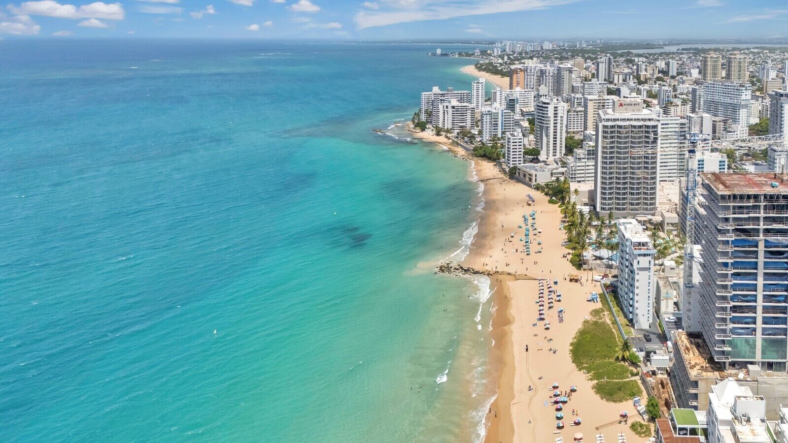 A coastal cityscape with a beach, high-rise buildings, and clear blue waters.