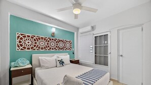 Een slaapkamer met een bed, nachtkastjes, een plafondventilator, een decoratief wandpaneel, een raam met zonwering en een deur.