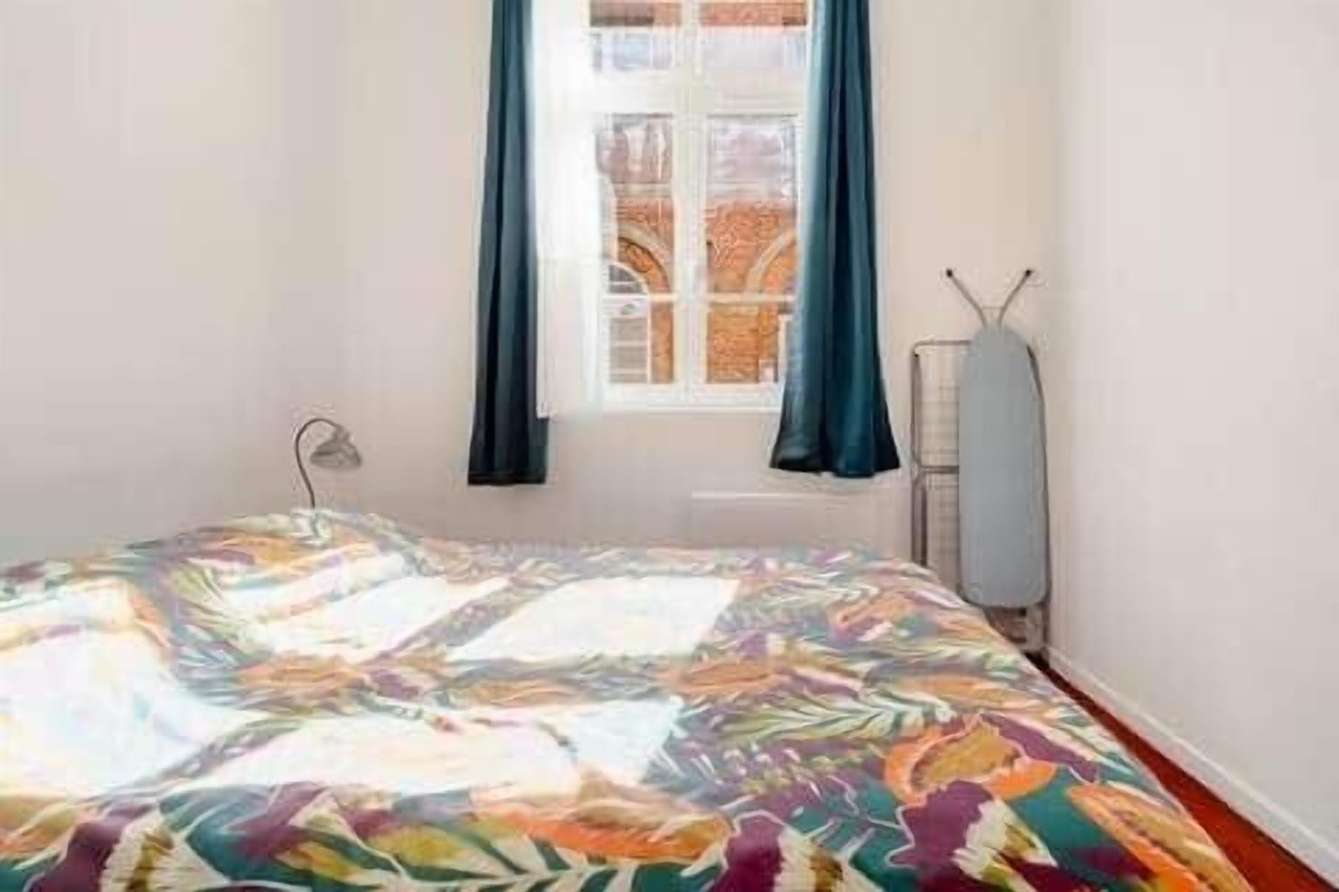 Un dormitorio con cama, ventana con cortinas y un radiador.