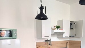A compact kitchen with a washing machine, oven, microwave, and a hanging light fixture. - Authentic apartment - Historic Orbec (Orbec)