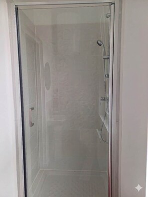 Een douche met glazen wanden, een handdouche en een wandmengkraan.