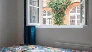 A room with a bed, a window, and a view of a brick building. - Authentic apartment - Historic Orbec (Orbec)
