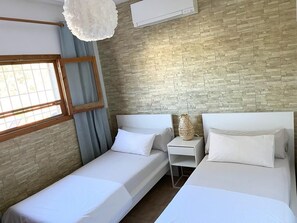 A hotel room with two single beds, a small bedside table with a lamp, and a window with curtains.