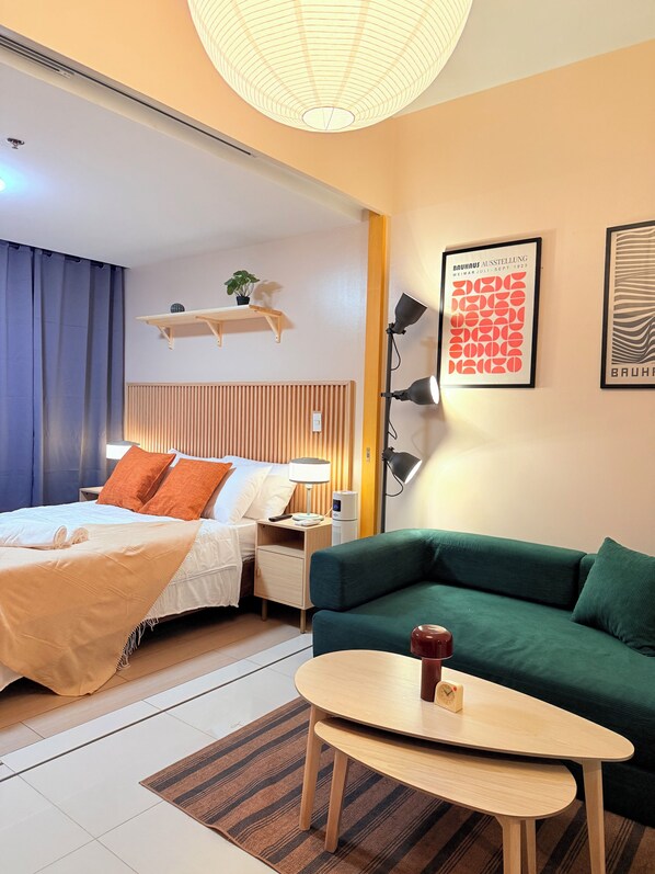 Ein Hotelzimmer mit einem Bett, einem grünen Sofa, einem kleinen Tisch, einer Lampe und einem an der Wand befestigten Regal mit einer Pflanze.
