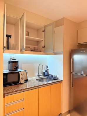 Eine kleine Küche mit integriertem Mikrowellenherd, Toaster, Spüle und einem Edelstahlkühlschrank.