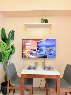 Ein Essbereich mit an der Wand montiertem Fernseher, Tisch mit Stühlen, einem Blumentopf und einem Regal über dem Fernseher.