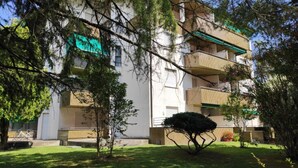 A multi-story building with balconies, a bicycle parked outside, and a well-maintained lawn. - Central Flat With Covered Terrace (Lignano Sabbiadoro)