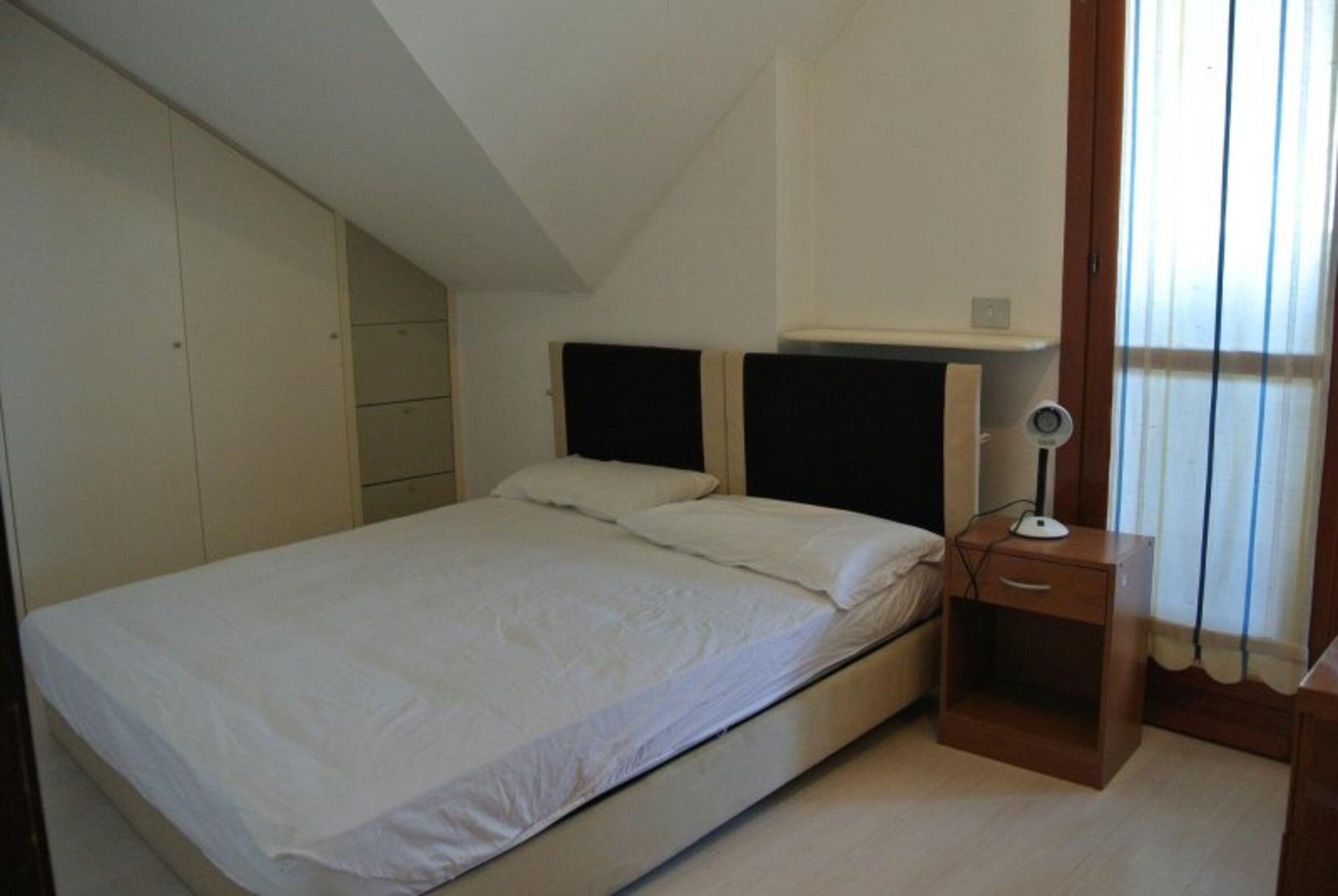 A bedroom with a single bed, a nightstand, a desk, and a wardrobe.