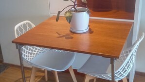 Ein Holztisch mit zwei weißen Stühlen, einer Topfpflanze und einem Regal mit Dekoration.