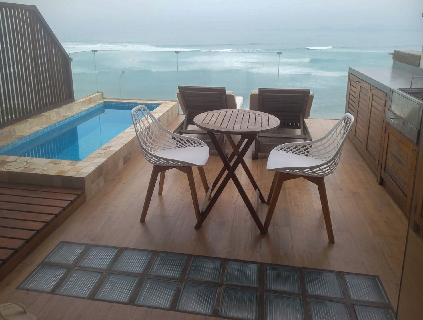 A poolside area with a view of the ocean, a table with chairs, and a grill.