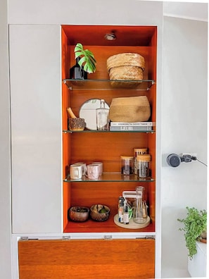 A kitchen cabinet with shelves containing kitchenware, a plant, and a book titled 'COOKING for GOOD TIMES.' - Oceanview 2BR & Terrace in Punta Hermosa (Punta Hermosa)