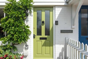 A green door with a black knocker, a white picket fence, and a mailbox on the white brick wall. - Cosy Sussex Cottage (Robertsbridge, Staplecross)