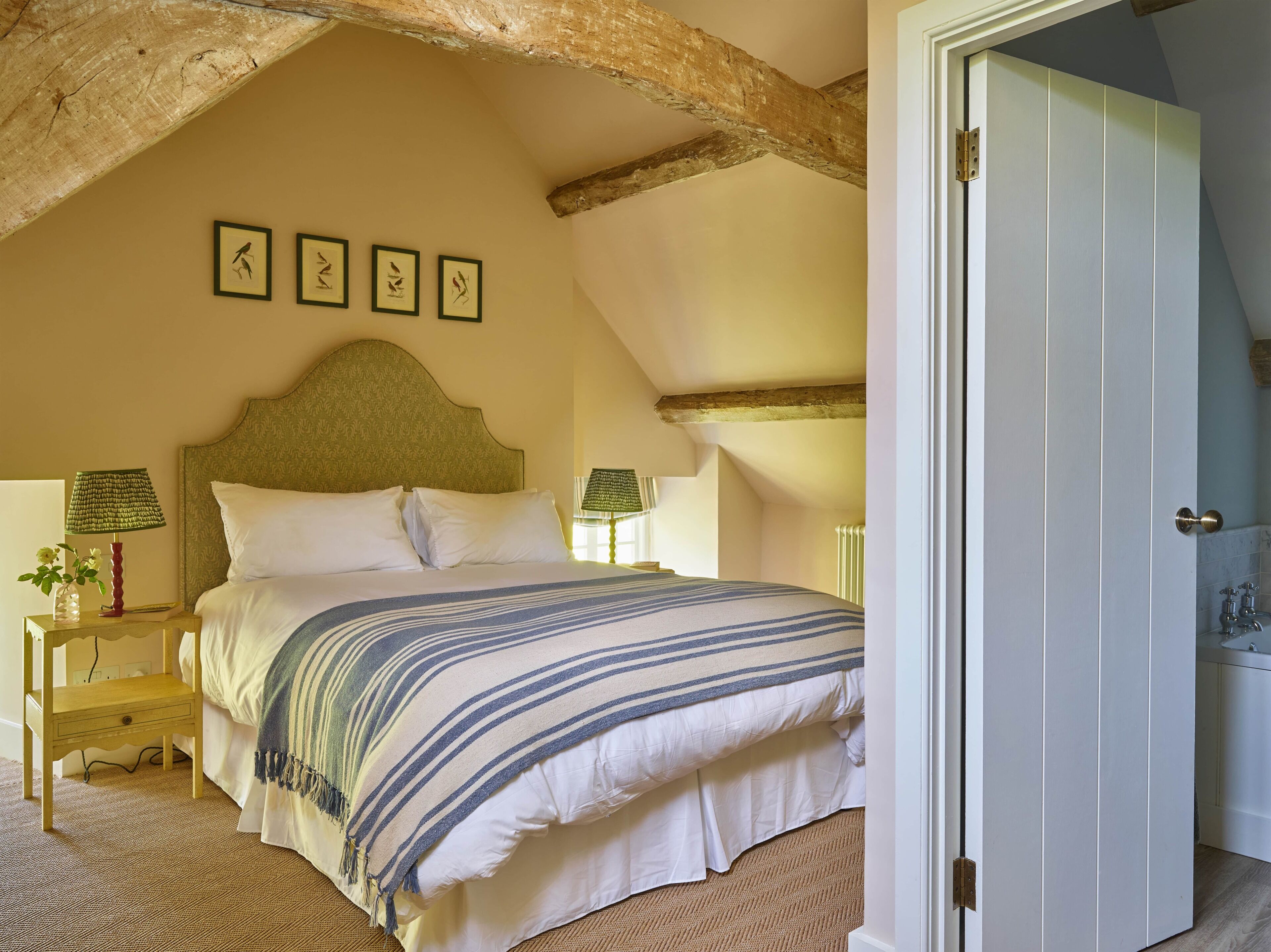 Un dormitorio con cama, dos mesitas de noche, una viga de techo de madera y una puerta al baño.