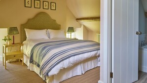 A bedroom with a bed, two bedside tables, a wooden ceiling beam, and a door to a bathroom. - Stancombe Farmhouse, an idyllic Cotswold retreat set in its own private valley (Dursley)