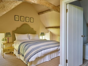 A bedroom with a bed, two bedside tables, a wooden ceiling beam, and a door to a bathroom.