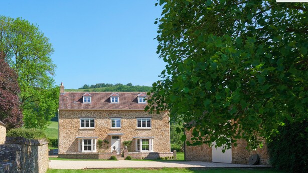 A stone house with a tiled roof, a front door, and a paved driveway. - Stancombe Farmhouse, an idyllic Cotswold retreat set in its own private valley (Dursley)
