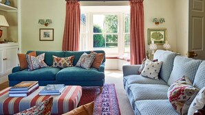 A living room with two sofas, a coffee table, and a bookshelf. - Stancombe Farmhouse, an idyllic Cotswold retreat set in its own private valley (Dursley)