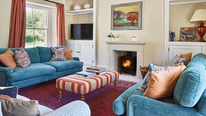 A cozy living room with a fireplace, a sofa, a television, and a bookshelf. - Stancombe Farmhouse, an idyllic Cotswold retreat set in its own private valley (Dursley)