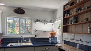 A kitchen with a sink, wooden cabinets, a window with a view, and shelves with kitchenware. - Dave's place 3-bedroom cozy cottage in downtown Grand Marais, MI (Grand Marais)
