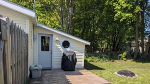 A small, single-story building with a front door, a covered outdoor seating area, and a wooden deck. - Dave's place 3-bedroom cozy cottage in downtown Grand Marais, MI (Grand Marais)