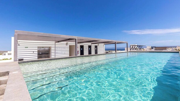 Ein moderner Poolbereich mit einem klaren, blauen Pool, einer überdachten Sitzgelegenheit und Blick auf den Ozean.