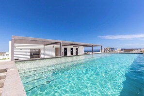 Un área moderna junto a la piscina con una piscina azul cristalina, una zona de estar cubierta y vista al océano.