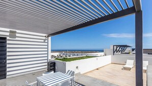 Eine Dachterrasse mit Tisch und Stühlen, Blick auf das Meer und ein überdachter Bereich mit einer Pergola.