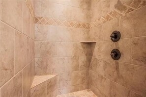 A shower area with beige tiles, a corner shelf, and two wall-mounted shower controls. - AGGIELAND family HOME away from HOME (College Station)