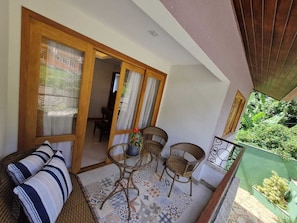 Ein Balkon mit Korbmöbeln, einem gemusterten Boden und Blick ins Grüne.