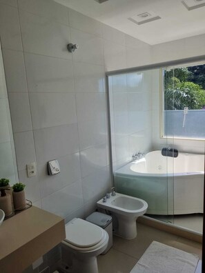 A modern bathroom with a bathtub, bidet, toilet, and a large mirror. - Casa Azaléia  (Teresópolis)