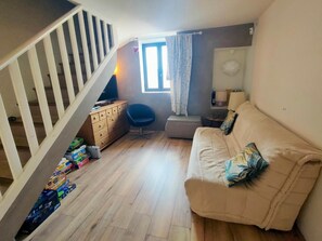 Ein Wohnzimmer mit Sofa, Sessel, Fernseher, Kommode und Fenster.