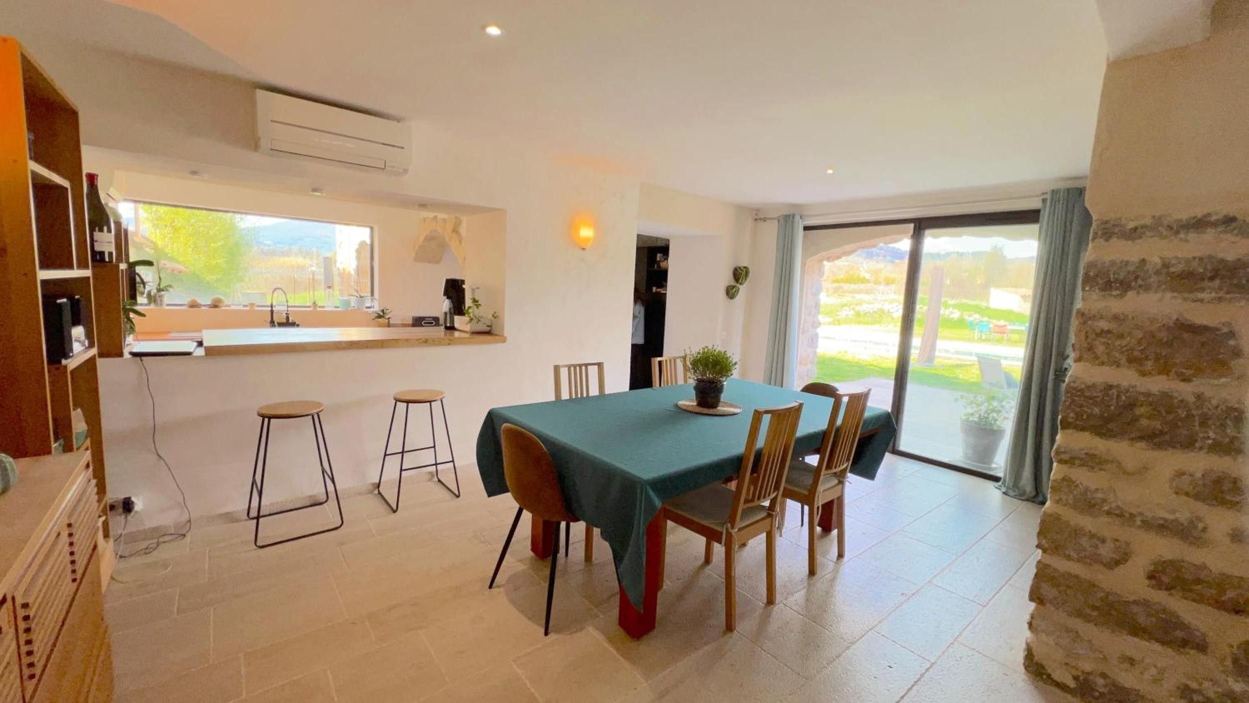 A dining area with a table set for four, a kitchen area with a window, and a view of a garden through the door.