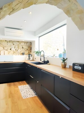 Cozinha moderna com painel de parede de pedra, uma janela grande e bancada de madeira.