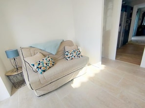 Ein beiges Sofa mit gemusterten Kissen, eine Stehlampe und ein kleiner Beistelltisch mit einem dekorativen Gegenstand.