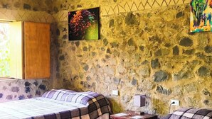 Quarto com duas camas, parede de pedra, pintura de flores e pintura de um elefante.