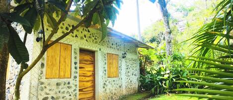 Un edificio de piedra con dos puertas y ventanas de madera, rodeado de abundante vegetación.