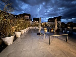 A rooftop terrace with potted plants, outdoor seating, and a modern building in the background. -  EXCEPTIONAL  APARTMENT BETWEEN LAKE AND MOUNTAINS (Annecy)