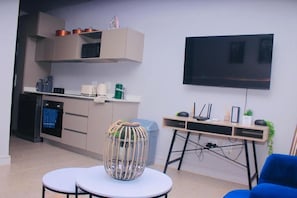 A modern kitchen with a microwave, oven, and cabinets, a dining area with a table and chairs, and a TV mounted on the wall. - Zimbali Lakes Boulevard Edge 103 (Ballito)
