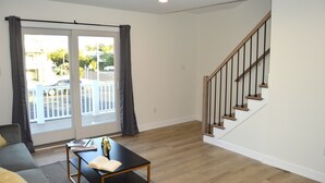 A living room with a sofa, a coffee table, a staircase, and a sliding glass door. - Amazing Luxury LBI Beach House - Rooftop Bay Views - Walk to Beach - Sleeps 14 (Ship Bottom)