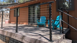 Une terrasse en bois avec une rambarde, une fenêtre et deux chaises bleues.