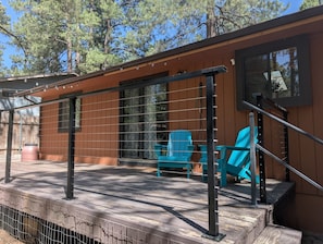 A wooden deck with a railing, a window, and two blue chairs. - New! Starlight Pines! Grill/AC/Dog Friendly! (Flagstaff)