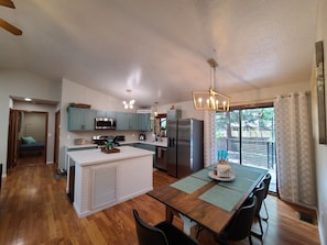 A modern kitchen with a central island, stainless steel appliances, and a dining area with a table and chairs. - New! Starlight Pines! Grill/AC/Dog Friendly! (Flagstaff)