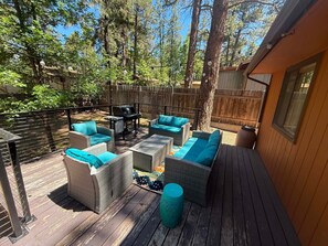 Une terrasse dotée de meubles en osier, d’un barbecue et offrant une vue sur les arbres.