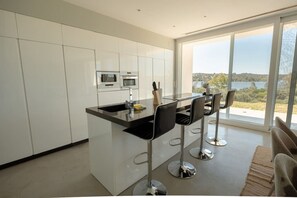 A modern kitchen with white cabinets, a black countertop, and stainless steel appliances. There are three bar stools with black seats and silver legs.