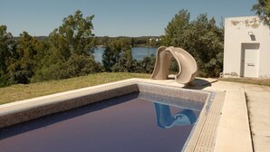 Une piscine agrémentée d’une sculpture originale, entourée d’arbres et offrant une vue sur un lac.